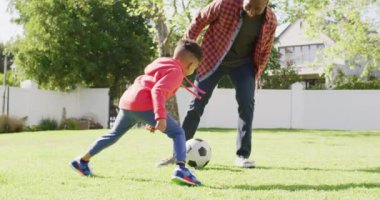Happy african american father and his son playing football in garden. Spending quality time at home.