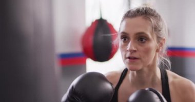 Video of confident, determined caucasian woman in boxing gloves training with punchbag at a gym. Exercise, fitness and healthy lifestyle.