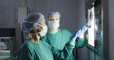 Video of two diverse female surgeons discussing x-ray on lightbox in operating theatre. Hospital, medical and healthcare services.