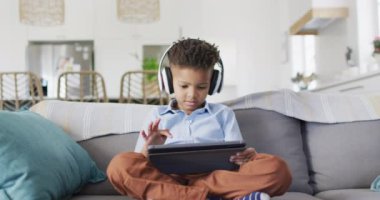 Happy african american boy sitting on sofa and using tablet. Spending quality time at home, childhood and technology concept.