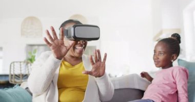 Heyecanlı Afro-Amerikan büyükannesi evde torunuyla otururken VR kulaklık kullanıyor. Teknoloji, iletişim, öğrenme, aile ve ev hayatı.