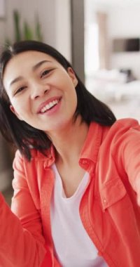 Vertical video of smiling biracial woman with dark hair waving to camera. Leisure time, communication, domestic life and lifestyle concept.