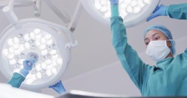 Low angle of biracial female surgical assistant preparing lights in operating theatre, copy space. Hospital, medical and healthcare services.