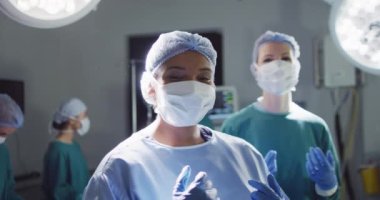 Video of smiling biracial female surgeon and diverse colleague in face masks in operating theatre. Hospital, medical and healthcare services.