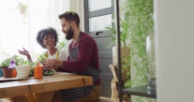Video of happy diverse couple tending to plants at home, with copy space. Happiness, inclusivity, free time, ecology, togetherness and domestic life.