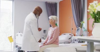 Steteskoplu Afrika kökenli Amerikalı erkek doktor, hastanedeki beyaz kadın hastayı muayene ediyor. Tıp, sağlık, yaşam tarzı ve hastane konsepti.