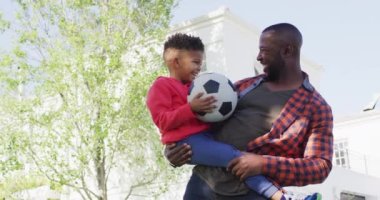 Portrait of happy african american father and his son holding football and embracing in garden. Spending quality time at home.