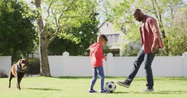 Happy african american father and his son playing football in garden. Spending quality time at home.