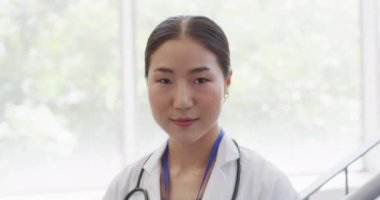 Video portrait of happy asian female doctor smiling in hospital corridor. Hospital, medical and healthcare services.