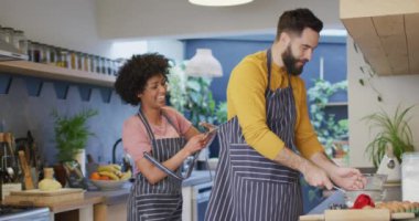 Video montage of happy diverse couple at home cooking, tending to plants and relaxing together. Happiness, communication, inclusivity, free time, togetherness and domestic life.