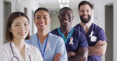 Video portrait of diverse group of smiling medical workers with cancer ribbons in hospital corridor. Hospital, medical and healthcare services.
