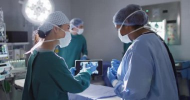 Video of two diverse female surgeons discussing x-ray on tablet in operating theatre. Hospital, medical and healthcare services.