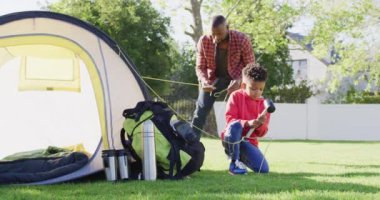 Happy african american father and his son setting up tent in garden. Spending quality time at home.