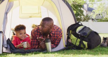 Happy african american father and his son laying in tent in garden. Spending quality time at home.