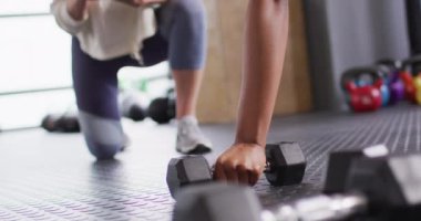 Video of diverse female fitness trainer and determined woman raising dumbbells working out at a gym. Exercise, fitness and healthy lifestyle.