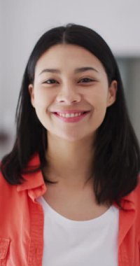 Vertical video of smiling biracial woman with dark hair looking at camera. Leisure time, domestic life and lifestyle concept.