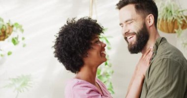 Video portrait of happy diverse couple in living room embracing and smiling, with copy space. Happiness, inclusivity, free time, togetherness and domestic life.