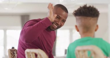 Happy african american man and his son sitting at table and high-fiving. Spending quality time at home, childhood, deafness and family concept.