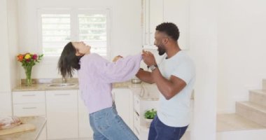 Happy diverse couple holding hands and dancing in kitchen. Spending quality time at home concept.