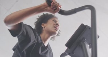 Low angle video of tired african american woman on exercise bike working out at a gym. Exercise, fitness and healthy lifestyle.