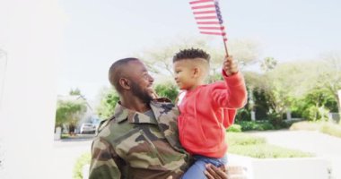 Happy african american father with son embracing and waving flag of usa. Global patriotism and family concept.