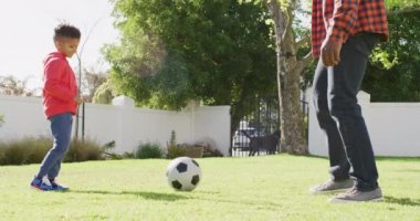 Happy african american father and his son playing football in garden. Spending quality time at home.