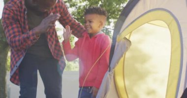 Happy african american father and his son setting up tent and high-fiving in garden. Spending quality time at home.