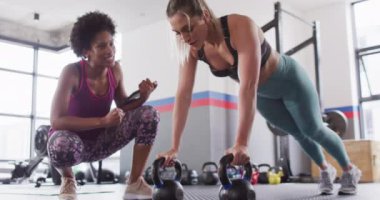 Video of diverse female fitness trainer encouraging woman doing push ups on kettlebells at gym. Exercise, fitness and healthy lifestyle.