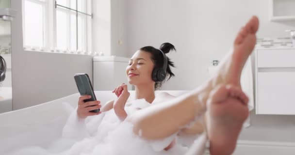 Video Portrait Smiling Biracial Woman Headphones Smartphone Bathtub Bubble Bath — Stok video