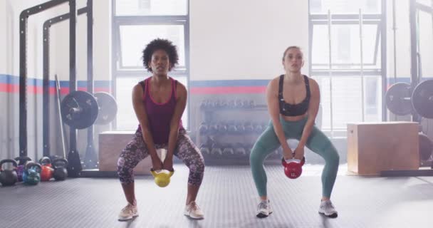 2人の多様な女性がジムで一緒にケトルベルのスイングをしているビデオ フィットネス 健康的なライフスタイル — ストック動画