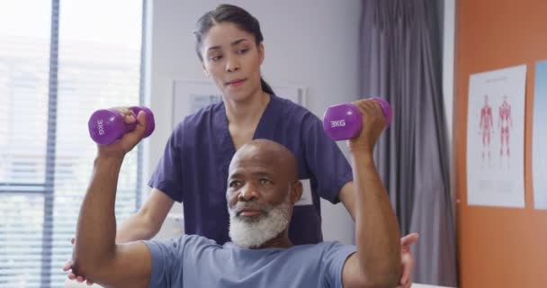 Fisioterapeuta Feminina Diversa Paciente Masculino Sênior Segurando Halteres Sessão Fisioterapia — Vídeo de Stock