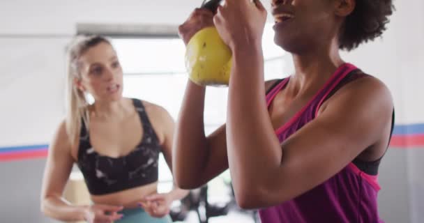 ジムでケトルベルの重さでスクワットをする女性を奨励する多様な女性フィットネストレーナーのビデオ フィットネス 健康的なライフスタイル — ストック動画