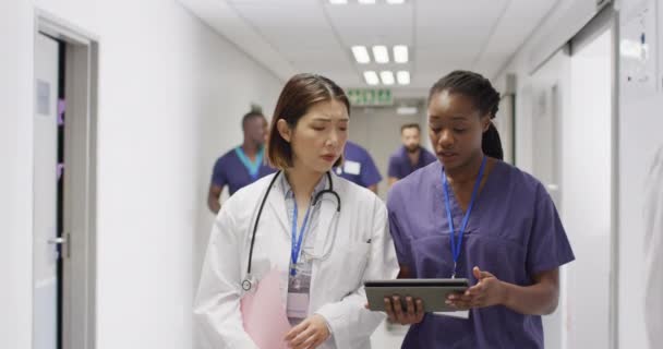 Nagranie Dwóch Różnych Lekarzy Spacerujących Ruchliwym Korytarzu Szpitalnym Patrzących Tabliczkę — Wideo stockowe