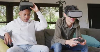 Happy diverse male teenage friends playing video games and using vr headsets at home, slow motion. Spending quality time at home together.