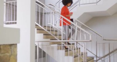 Mutlu Afro-Amerikan iş adamı merdivenlerden inip ofisinde kahve tutuyor, ağır çekim. Modern ofis, iş ve finans sektöründe çalışmak.