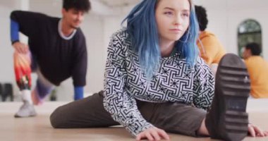 Caucasian female dancer stretching with diverse colleagues in dance studio, slow motion. Hobby, art and dance studio concept.