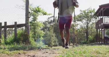 Senior african american man hiking with trekking poles on sunny day, slow motion. Hiking, active lifestyle and nature concept.