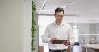 Kafkas işadamı ofisinde tablet kullanarak ağır çekimde yürüyor. Modern ofis, iş ve finans sektöründe çalışmak.