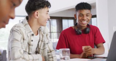Three happy diverse male teenage friends using laptop and talking at home, slow motion. Spending quality time at home together.