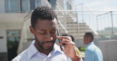 Ofiste akıllı telefondan konuşan mutlu Afro-Amerikan işadamı, ağır çekimde. Modern ofis, iş ve finans sektöründe çalışmak.