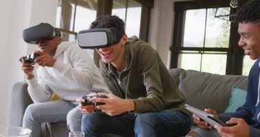 Happy diverse male teenage friends playing video games and using vr headsets at home, slow motion. Spending quality time at home together.