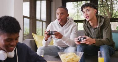 Happy diverse male teenage friends playing video games at home, slow motion. Spending quality time at home together.