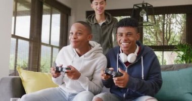 Happy diverse male teenage friends playing video games at home, slow motion. Spending quality time at home together.