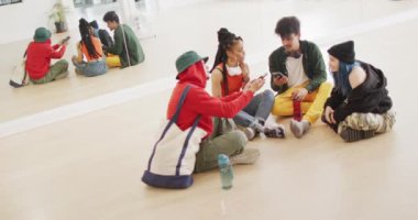 Happy diverse male and female dancers talking and using smartphone in dance studio, slow motion. Hobby, art and dance studio concept.