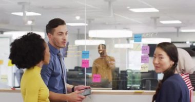 Bir grup iş adamı cam duvara notlar alıyor ve ofiste konuşuyorlar, ağır çekimde. Küresel iş, finans ve modern ofiste çalışma.