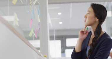 Asyalı iş kadını ofisteki cam duvara not alıyor, ağır çekimde. Küresel iş, finans ve modern ofiste çalışma.