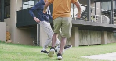 Happy diverse male teenage friends playing football in garden, slow motion. Spending quality time at home together.