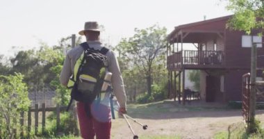 Senior african american man hiking with trekking poles on sunny day, slow motion. Hiking, active lifestyle and nature concept.