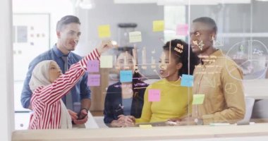 Bir grup iş adamı cam duvara notlar alıyor ve ofiste konuşuyorlar, ağır çekimde. Küresel iş, finans ve modern ofiste çalışma.