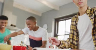 Happy diverse male teenage friends preparing pizza in kitchen, slow motion. Spending quality time at home together.